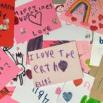 An overhead picture of valentines cards spread out on a table. They are handwritten and multicolored, with handmade drawings.